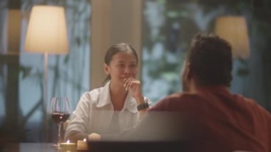Neşeli Asyalı kadın partneriyle sohbet ediyor ve akşam evde romantik bir akşam yemeğinde gülümsüyor.