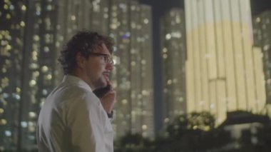 Beyaz iş adamının resmi kıyafetleri şehirde gece açık havada dururken ve cep telefonuyla konuşurken belini kaldır.