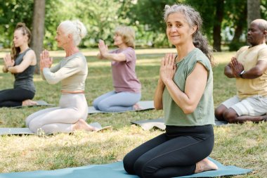 Dışarıda yoga dersinde meditasyon yaparken kameraya bakan son sınıf kadınının portresi.