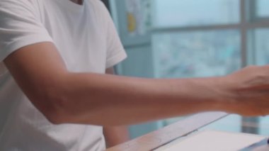 Stüdyoda iş yerindeki kağıt üzerine resim çizerken suluboya boya ve fırça kullanan genç Asyalı ressamın yatay çekimini kapat