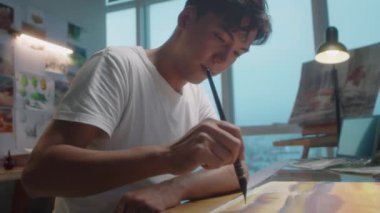 Sanat stüdyosunda çalışırken genç Asyalı bir adamın resim çizerken orta seçmeli bir fotoğrafı.