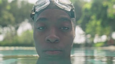 Profesyonel siyah yüzücü portresi şapkalı ve kafasının üstünde gözlüklü havuz suyunda kameraya poz veriyor.