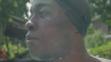 Yüzme gözlüğü takan ve açık havuzda kameraya poz veren ıslak tenli siyah bir adamın portresi.