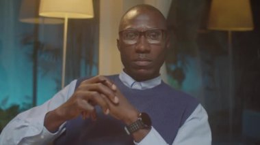 Akşamları ofisinde otururken kameraya poz veren ciddi bir Afrikalı Amerikalı psikoloğun portresi