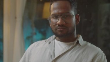 Kendine güvenen gözlüklü, çenesini ovuşturan ve ofiste kameraya poz veren erkek terapistin göğüs portresi.