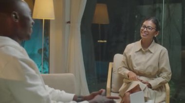 Afrikalı Amerikalı bir adam Asyalı bir kadın psikoloğun elini sıkıyor ve akşam terapi seansı sırasında onunla konuşuyor.