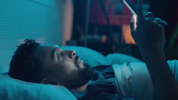 Young Bearded Man Lying Bed Dark Room Browsing Mobile Internet — Stock Video