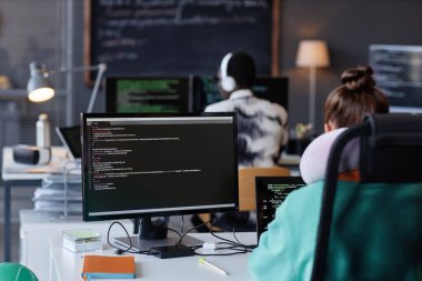 İş yerlerinde bilgisayarlarla oturan ve programla çalışan gençlerin arka görünümü