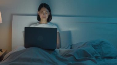 Genç bir kadının gece yatmadan önce evde oturup dizüstü bilgisayarda çalışırken orta boy bir fotoğrafı.