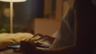 Küçük Asyalı kızın akşamları yatakta oturup dijital tablet kullanırken yakın çekim görüntüsü.