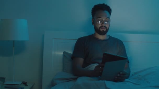 用数码平板电脑拍摄的大胡子青年男子的中景照片 然后把它放在一边 躺在床上 晚上回家睡觉 — 图库视频影像