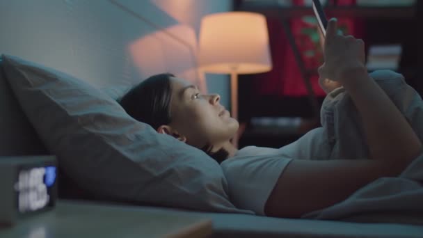 Молодая Женщина Использует Мобильный Телефон Постели Затем Лежит Одеялом Засыпает — стоковое видео