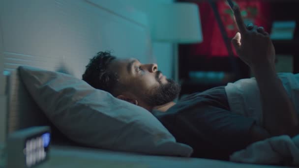 一个留着胡子的年轻人在床上用手机 然后躺在毯子下 晚上睡觉 — 图库视频影像