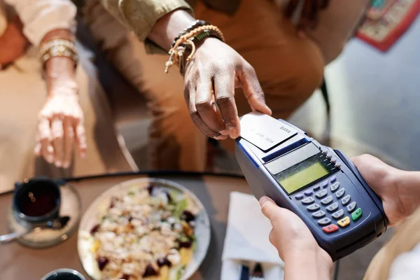 High angle view of customer paying for lunch with credit card while waiter holding terminal