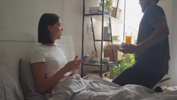 年轻女人在家里 一边用智能手机一边爱着丈夫 一边在床上为她端早餐 — 图库视频影像
