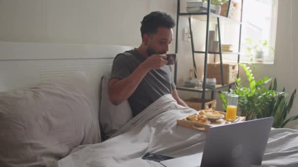 Νεαρός Τρώει Πρωινό Στο Κρεβάτι Πίνει Καφέ Τρώει Γλυκά Και — Αρχείο Βίντεο