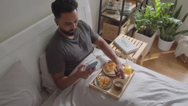 Genç Adamın Kahve Içerken Cep Telefonu Kullanırken Sabahları Yatakta Kahvaltı — Stok video