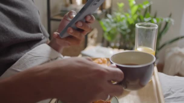 Genç Adamın Kahve Içerken Akıllı Telefon Kullanırken Sabahları Yatakta Kahvaltı — Stok video