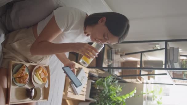 Pionowe Ujęcie Młodej Kobiety Jedzącej Śniadanie Łóżku Pijącej Sok Pomarańczowy — Wideo stockowe