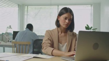 Diz üstü bilgisayarda çalışan ve ofiste not alan zarif resmi olan genç bir iş kadınının orta boy fotoğrafı.