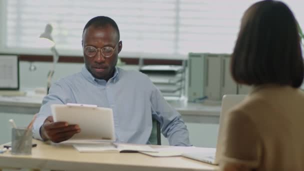 クリップボードでCvを読み オフィスの就職インタビュー中に女性候補者と話すアフリカ系アメリカ人男性Hrマネージャーの中型ショット — ストック動画