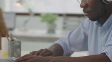 Ofis masasında dizüstü bilgisayar başında müzik dinlerken, kablosuz kulaklıkla Afrikalı Amerikalı iş adamının yakın plan fotoğrafını çek.