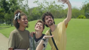Genç neşeli arkadaşlarının selfie çekerken orta boy fotoğrafı ve sonra yaz günü parkta akıllı telefondan resimlere bakması.