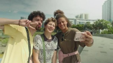 Neşeli Z arkadaşlarının selfie çektiği orta boy bir fotoğraf ve sonra yaz günü şehirde yürüyüş yaparken akıllı telefondan fotoğrafları kontrol ediyorlar.