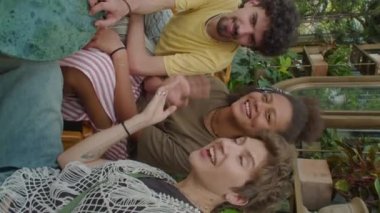 Yaz günü açık hava kafede oturan, gülümseyen, el sallayan ve sohbet eden gençlerin dikey pov görüntüleri sosyal medyada yayınlanırken veya internet araması yaparken.
