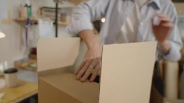 Karton kutuyu şeffaf bir bantla mühürlerken teslimat servisinde paket hazırlarken çekilmiş bir fotoğraf.
