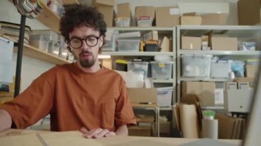 Telsiz kulaklıklı genç adamın laptopla video konuşması ve teslimat bürosunda çalışırken masasında notlar alırken orta boy görüntüsü.