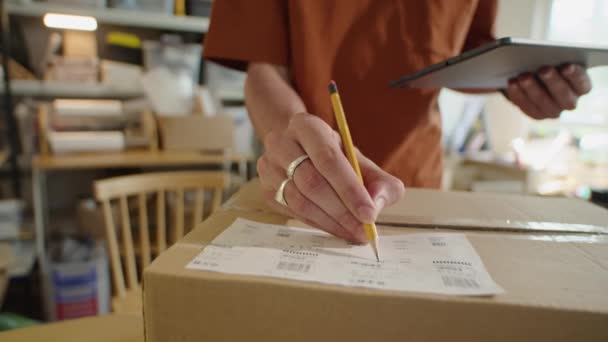 ラベルとデジタルタブレットで住所を書き 配送サービスオフィスの郵送物の小包を梱包しながら 認識できない男のクロップショット — ストック動画