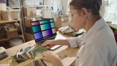 Kadın tasarımcı atölyede çalışırken dizüstü bilgisayar ekranında malzeme ve renk paletleri inceliyor
