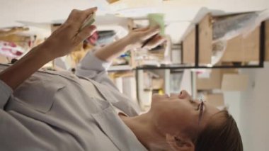 Yapışkan notların üzerine planları yazan ve onları depodaki duvara yapıştıran kadının dikey yan görüntüsü