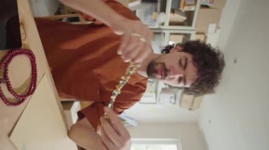 Genç adamın el yapımı boncuklu mücevher sergilediği ve dijital internet sitesi için DIY blogu ya da video reklamı çekerken kamerada konuştuğu dikey görüntü.