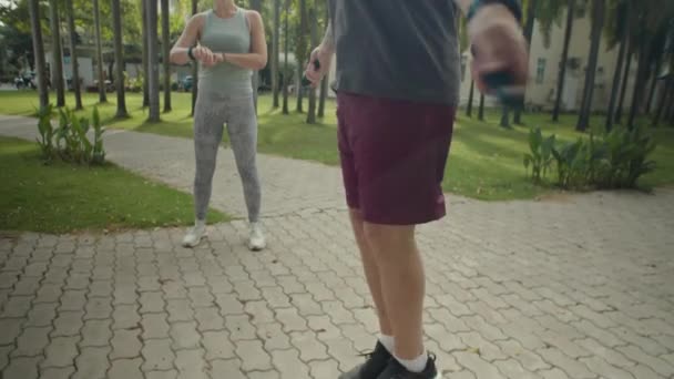 女性のパーソナルトレーナーが手をクラッピングし 公園の屋外トレーニング中に彼をサポートしながら スポーツウェアで男性のショットをトリミング — ストック動画