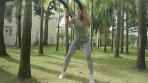 夏のアウトドアトレーニング中に公園でバトルロープ同期波を行うスポーツウェアの運動女性のスローモーションショットでズーム — ストック動画