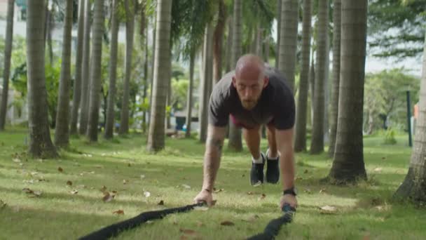 强壮的男子穿着运动服 夏天在公园里干活的时候 在绿草上拉起战绳 — 图库视频影像