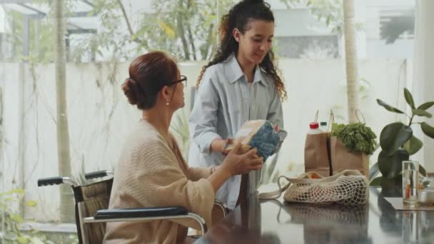 女社工卸下购物袋 与坐在轮椅上的资深亚洲妇女交谈 同时帮助她购买食物 — 图库视频影像