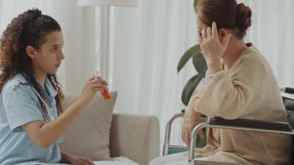 在家中向坐在轮椅上的资深亚洲妇女解释如何吃药的年轻女医生中的一个镜头 — 图库视频影像