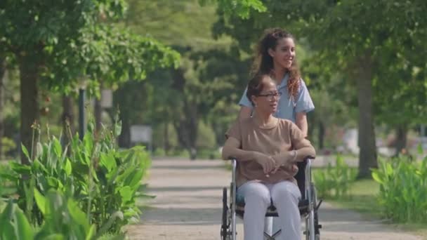 Πλήρης Εικόνα Της Νεαρής Γυναίκας Φροντιστή Σπρώχνει Ηλικιωμένη Ασιάτισσα Αναπηρικό — Αρχείο Βίντεο
