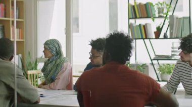 Bir grup dilsiz göçmen öğrenci, beyaz tahtada duran ve ders sırasında eğitim kartları gösteren bayan öğretmeni dinliyor.
