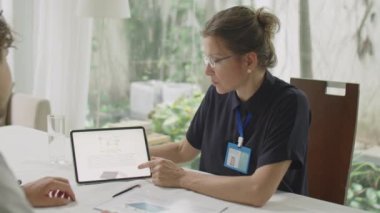 Kadın mühendisin dijital tablet üzerindeki sürdürülebilir enerji projesini ofis toplantısı sırasında erkek iş ortağına açıkladığı omuz üstünden.