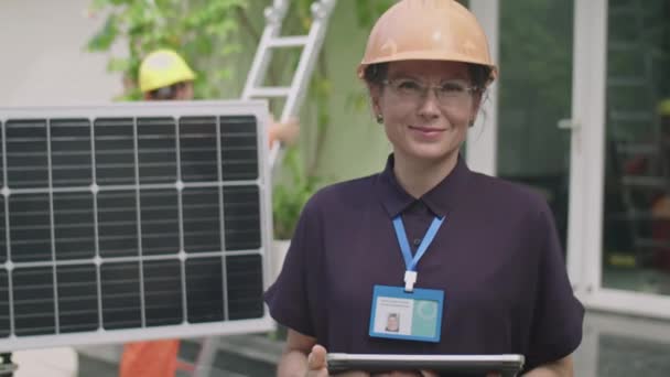 站在屋前太阳能电池板旁边 头戴硬帽 头戴数码平板相机的快乐女工程师站起来拍照 — 图库视频影像