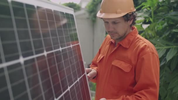 屋外に太陽電池パネルを設置している間 ワークウェアのプロの男性エンジニアのミディアムショット — ストック動画