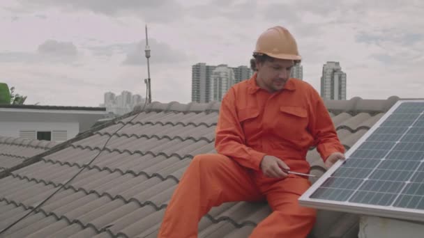 ワークウェアの男性技術者と屋上に座って 太陽電池パネルをインストールまたは固定しながらドライバーを使用して堅い — ストック動画