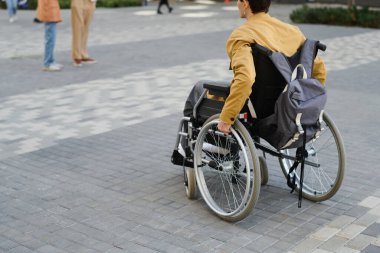 Sokakta hareket etmek için tekerlekli sandalye kullanan engelli bir gencin arka görüntüsü.