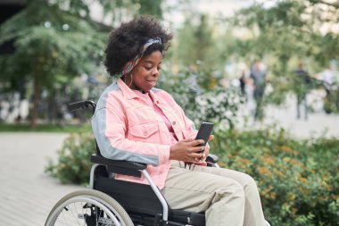 Engelli Afrikalı Amerikalı kadın dışarıda iletişim kurmak için akıllı telefonunu kullanıyor.