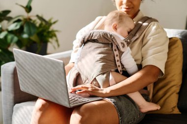 Kanepede bebeği askıda otururken internette çalışan bir kadın.