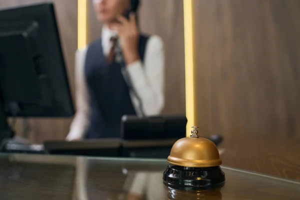 Close-up of bell on reception desk with administrator talking on the phone in background